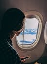 A woman looks out an airplane window, capturing a serene view of clouds and sky during a flight.