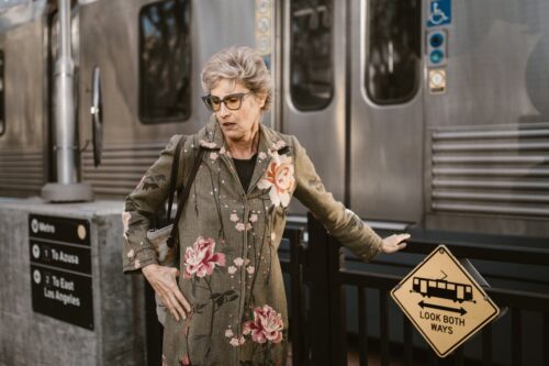 Elegant senior woman in floral coat waiting at Los Angeles metro station.